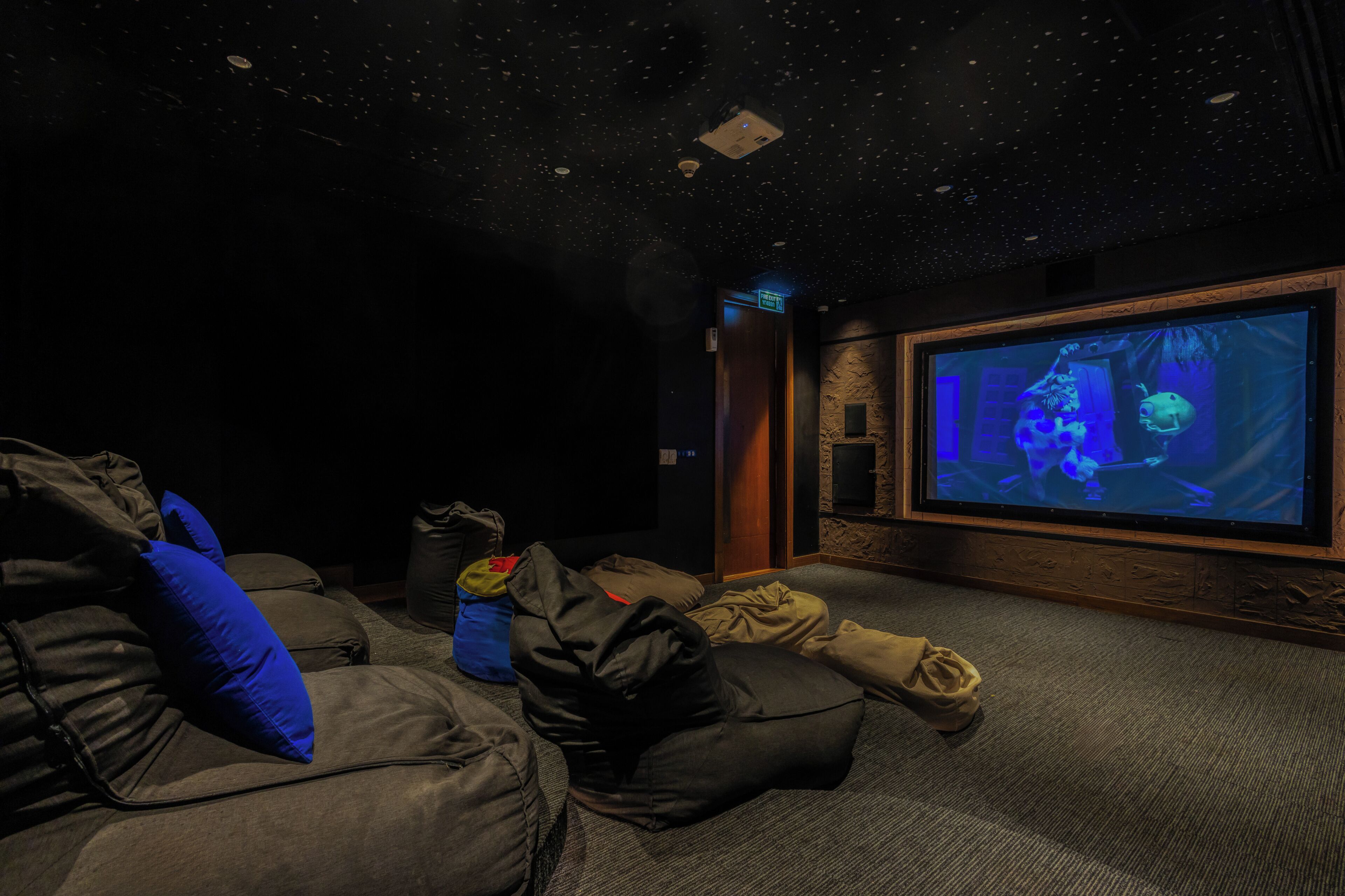 A dark room with a large screen displaying an underwater scene, a plush seating area, and a wall-mounted projector.