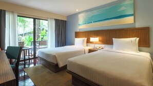 A hotel room with two beds, a desk, a chair, a lamp, and a painting of a beach scene.