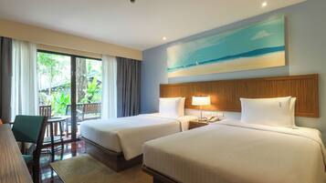 A hotel room with two beds, a desk, a chair, a lamp, and a painting of a beach scene.