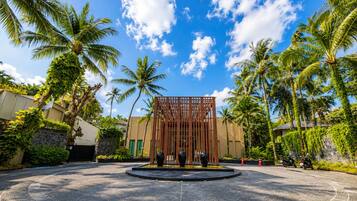 A circular driveway leading to a building with a wooden fence structure, surrounded by palm trees and a clear sky.