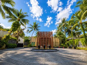 A circular driveway leading to a building with a wooden fence structure, surrounded by palm trees and a clear sky. - Holiday Inn Resort Phuket Surin Beach by IHG (Choeng Thale)