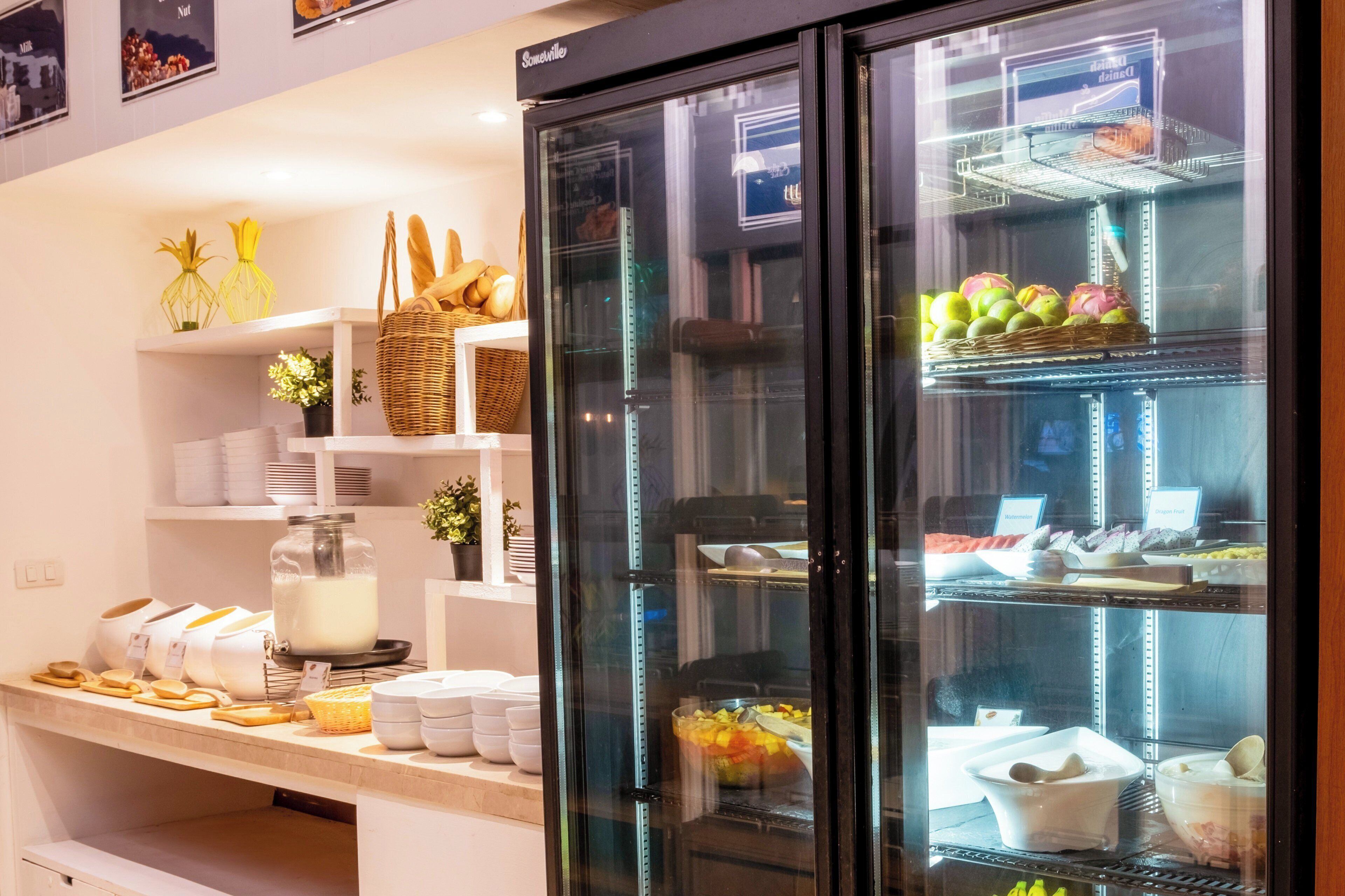 A breakfast buffet area with a variety of food items, including fruits and dairy products, displayed in a refrigerated case.