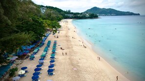 A beach with rows of umbrellas and chairs, a sandy shore, and a calm sea. - Holiday Inn Resort Phuket Surin Beach by IHG (Choeng Thale)