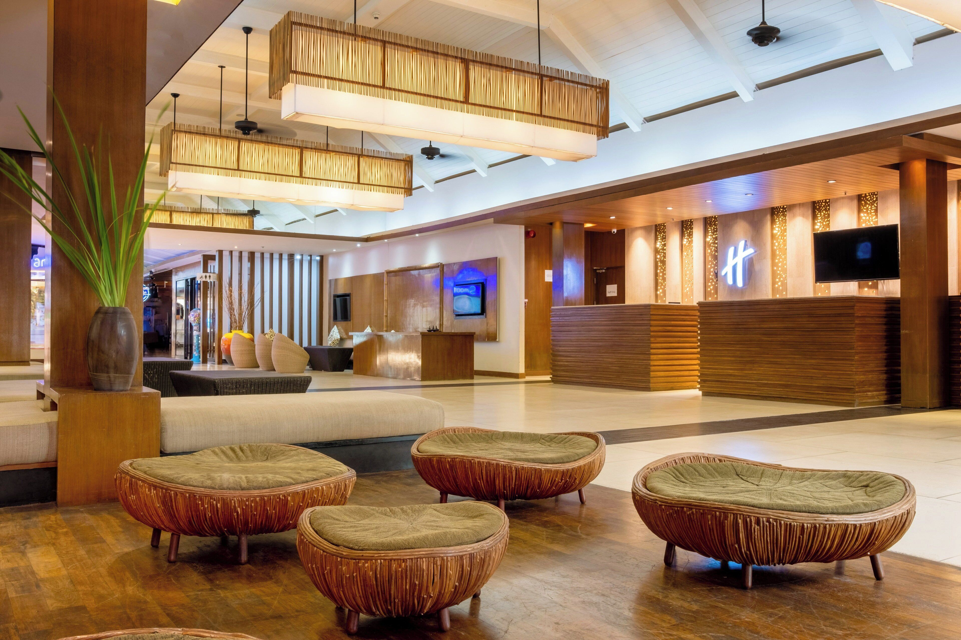 A spacious lobby with modern wicker furniture, a reception desk, and a large screen.
