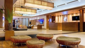 A spacious lobby with modern wicker furniture, a reception desk, and a large screen.