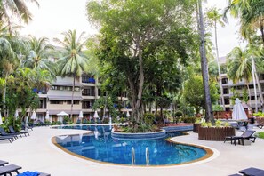 A resort pool area with lounge chairs, umbrellas, and a large tree in the center. - Holiday Inn Resort Phuket Surin Beach by IHG (Choeng Thale)