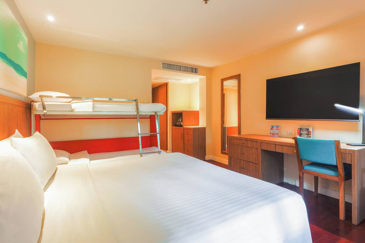 A hotel room with a bunk bed, a desk with a chair, a flat-screen TV, and a mirror.