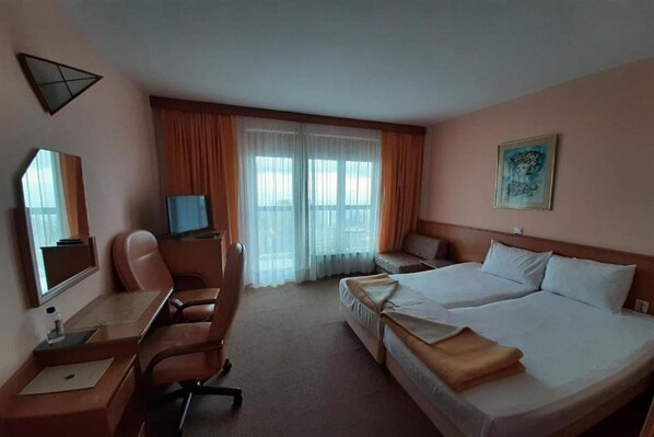Une chambre d’hôtel équipée d’un bureau, de deux lits, d’une chaise, d’un téléviseur et d’un tableau au mur.