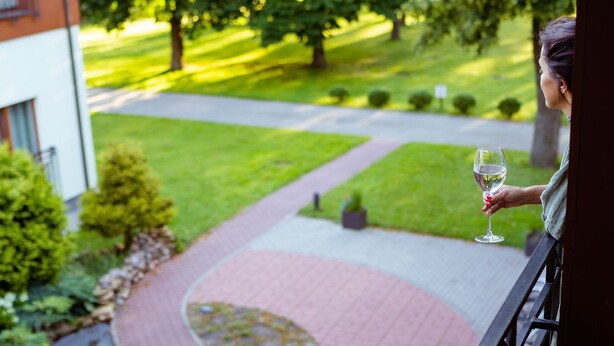 A balcony with a view of a landscaped garden and a building. - Regina Hotel (Druskininkai)