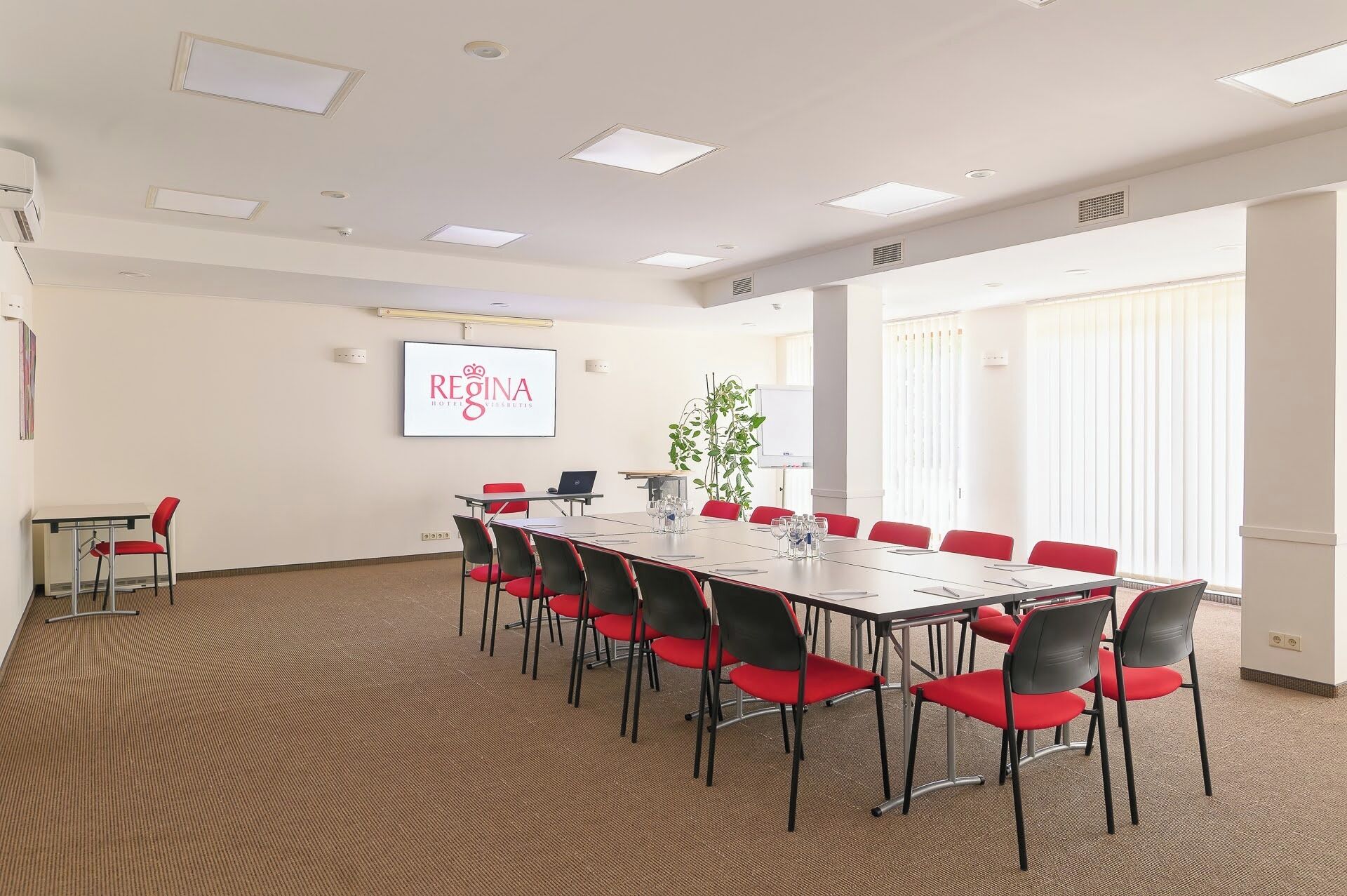 A conference room with a long table, red chairs, a projector screen, and a whiteboard.