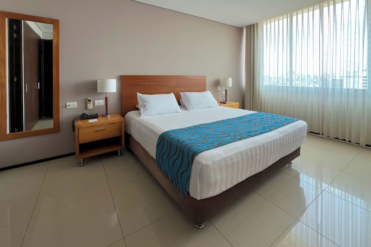 Una habitación de hotel con una cama grande, dos mesitas de noche, un espejo y una ventana con cortinas.