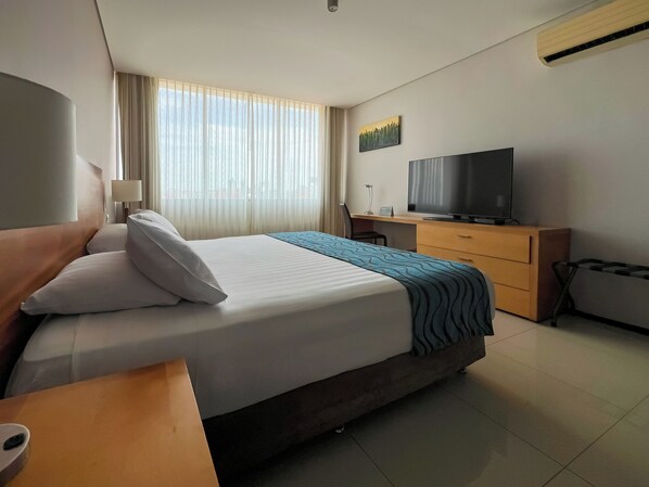 A hotel room with a bed, a desk, a television, and a window with curtains.