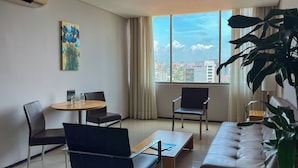 Una sala de estar moderna con un sofá, dos sillones, una mesita y un amplio ventanal con vistas a la ciudad.