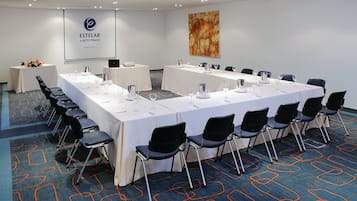A conference room with a long table, chairs, and a projector screen displaying 'ESTELAR EN ALTO PRADO'.