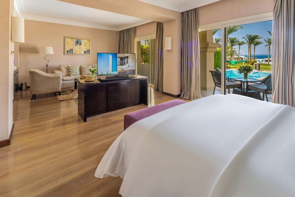 A hotel room with a large bed, a desk with a computer, a TV, and a view of a pool and palm trees.