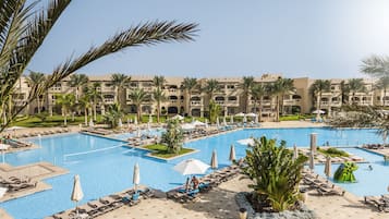 A large pool area with multiple swimming pools, sun loungers, umbrellas, and palm trees.