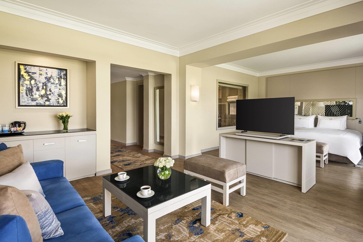 A hotel room with a sofa, coffee table, TV, and a bed.