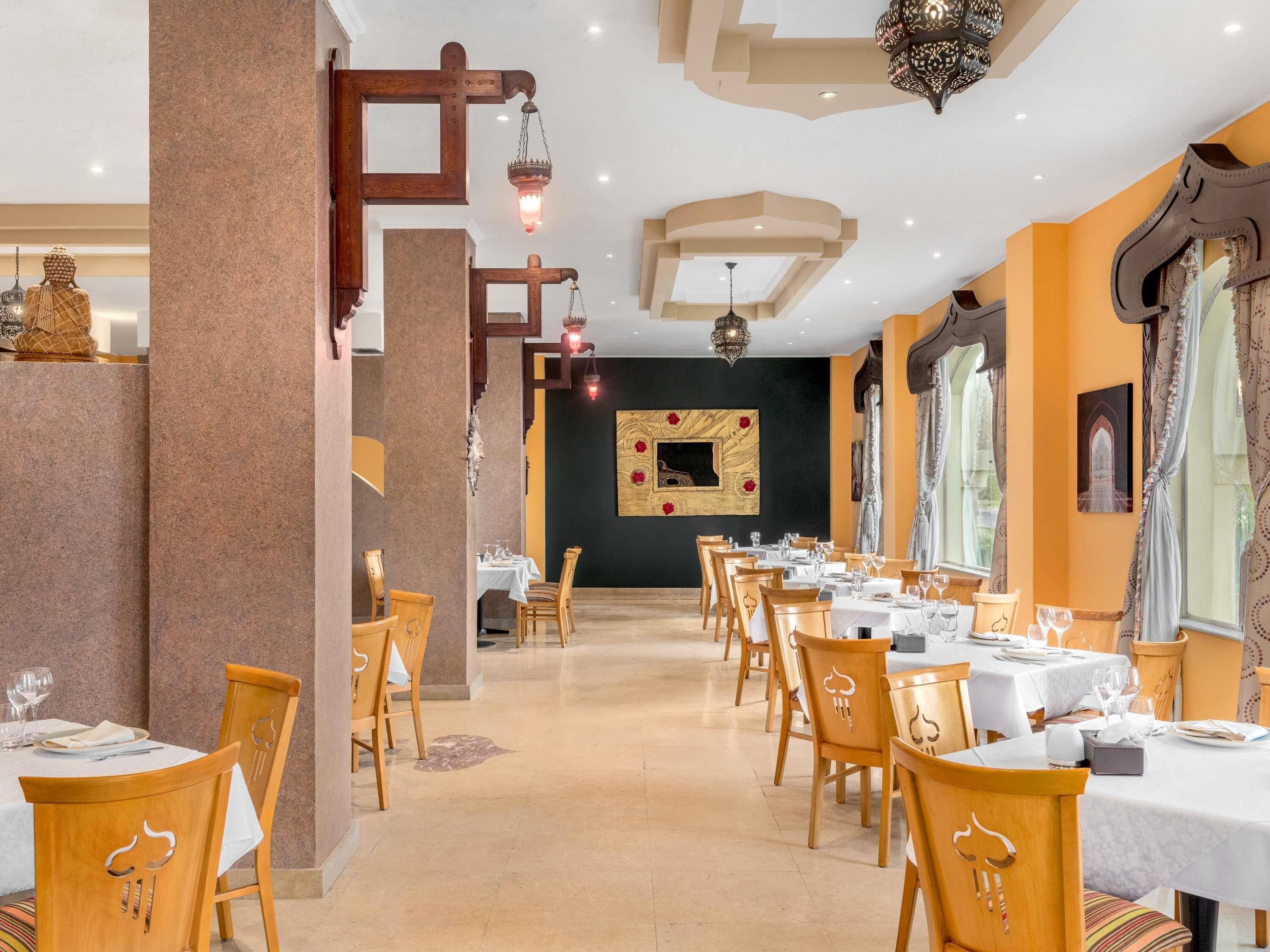A restaurant with wooden chairs and tables, a chandelier, and a wall-mounted artwork.