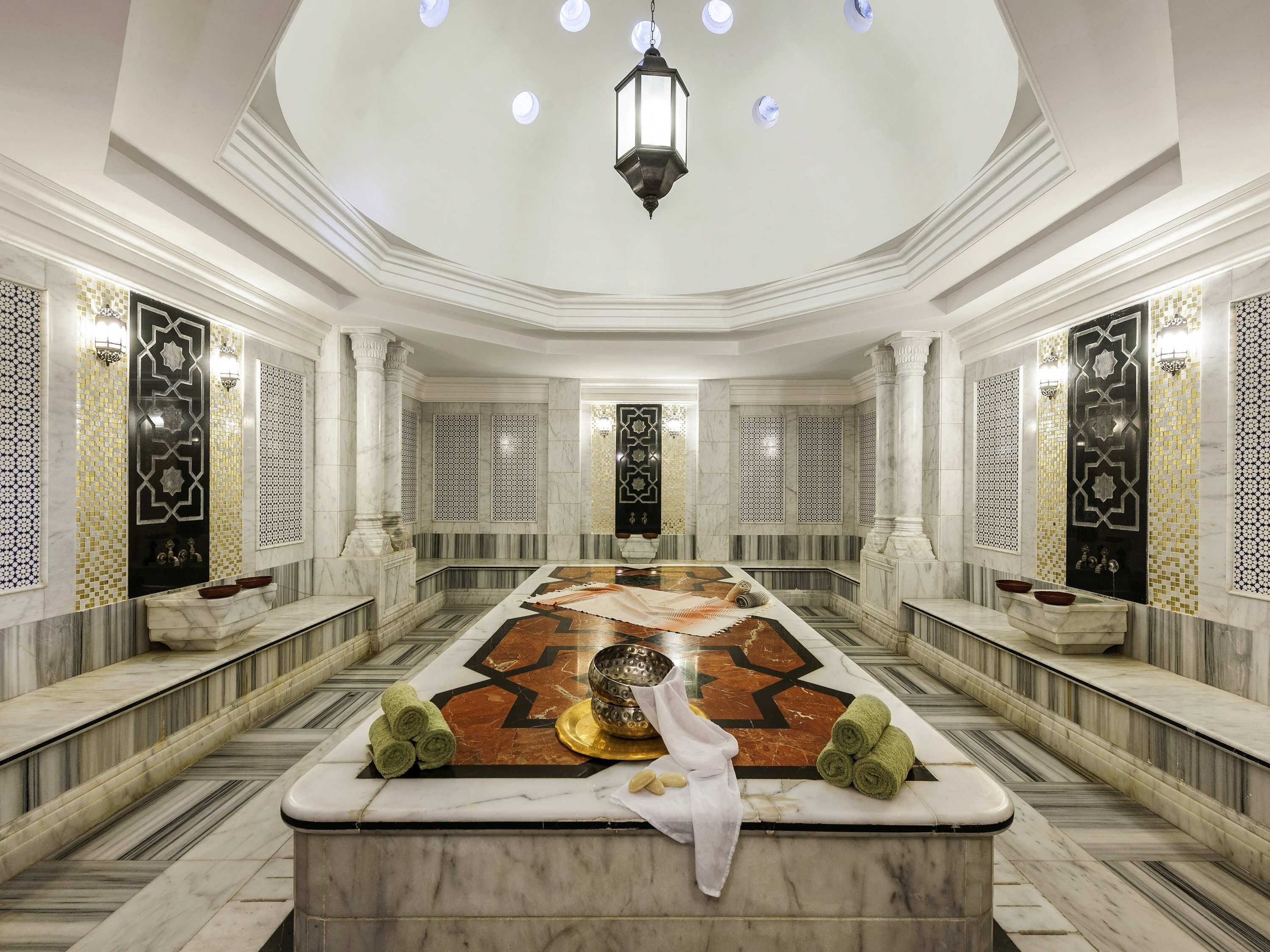A luxurious bathroom with a large marble vanity, a central decorative tile pattern, and a modern light fixture.