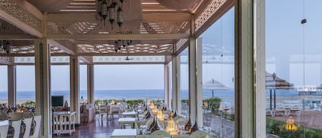 A covered outdoor dining area with tables set for a meal, overlooking the sea.