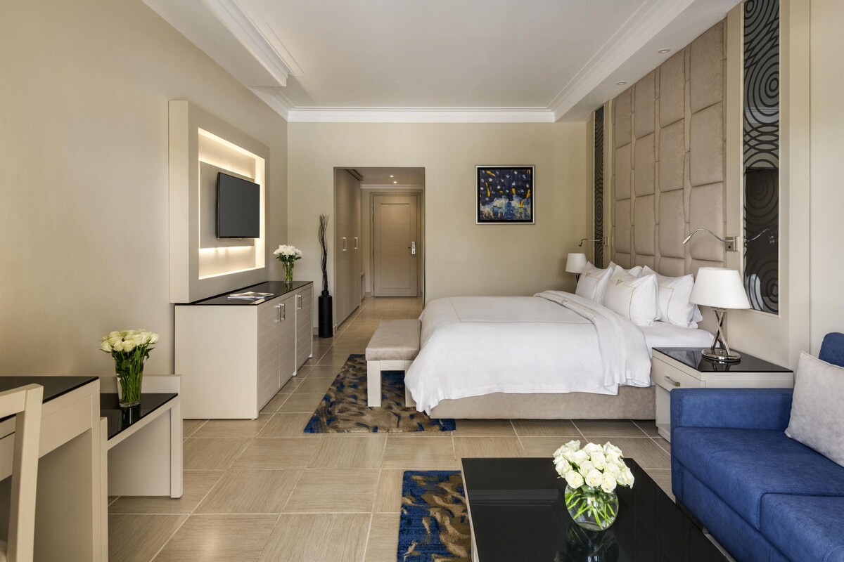 A hotel room with a bed, bedside table, TV, and a desk with a chair.