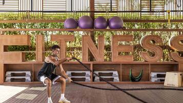 A man performing a workout with a battle rope in a wooden-floored area with a 'FITNESS' sign in the background.