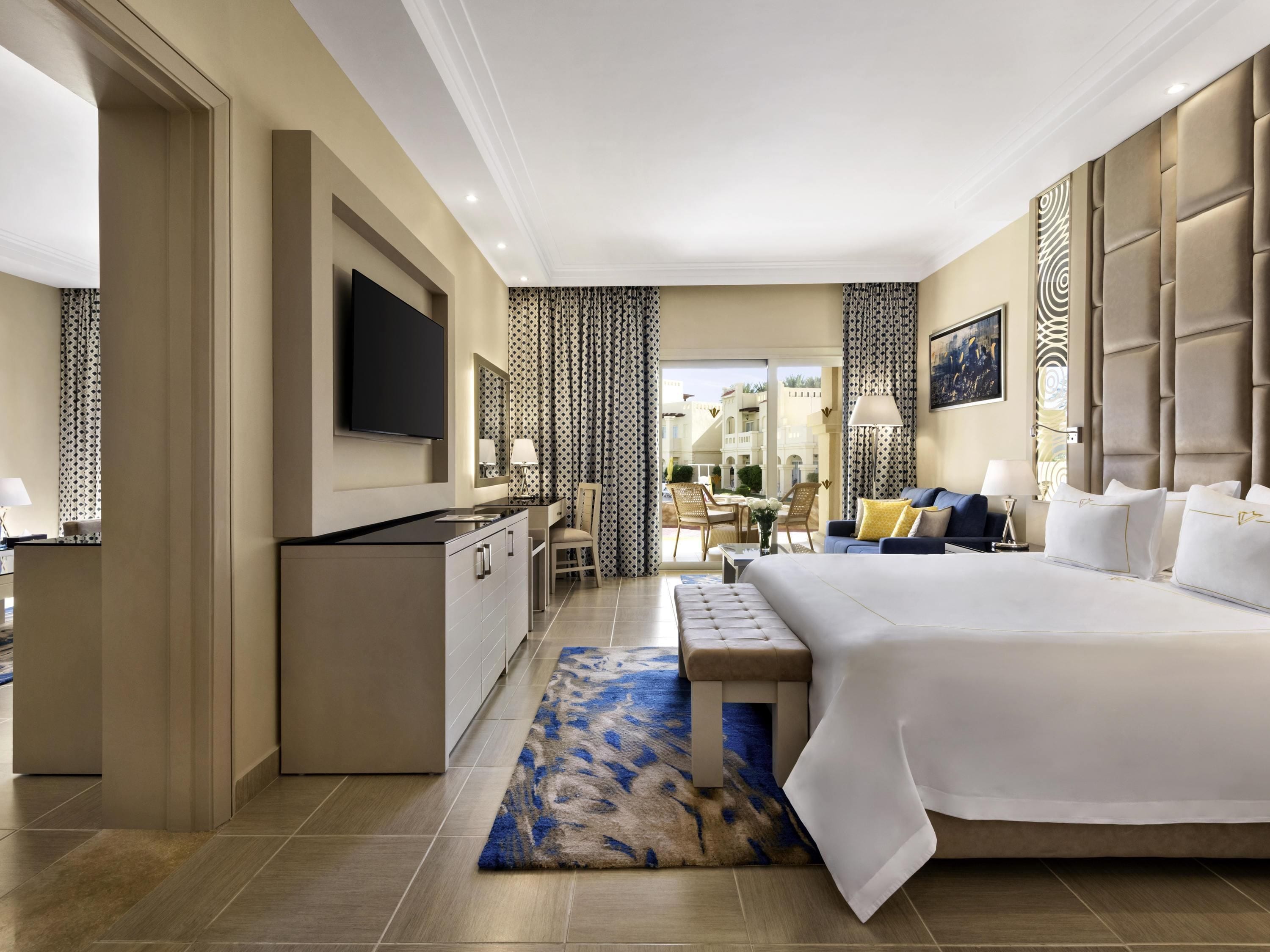 A hotel room with a large bed, a desk, a TV, and a view of the outside.