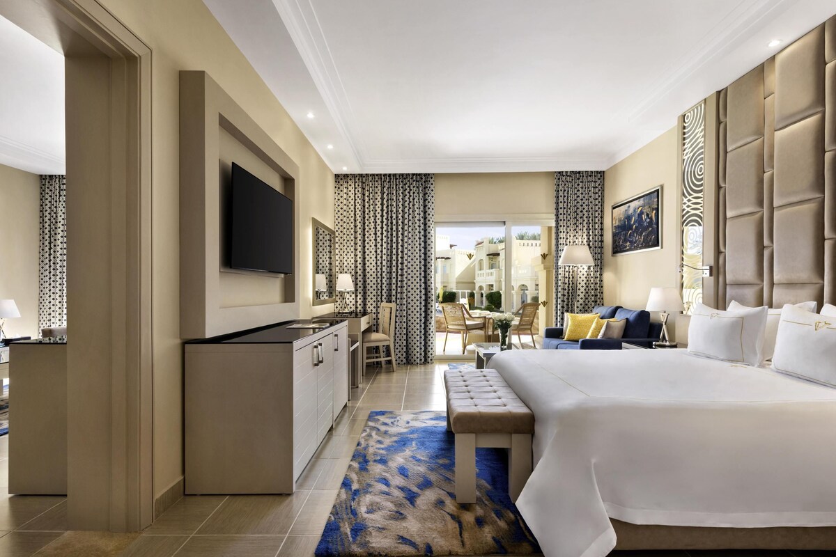A hotel room with a large bed, a desk, a TV, and a view of the outside.