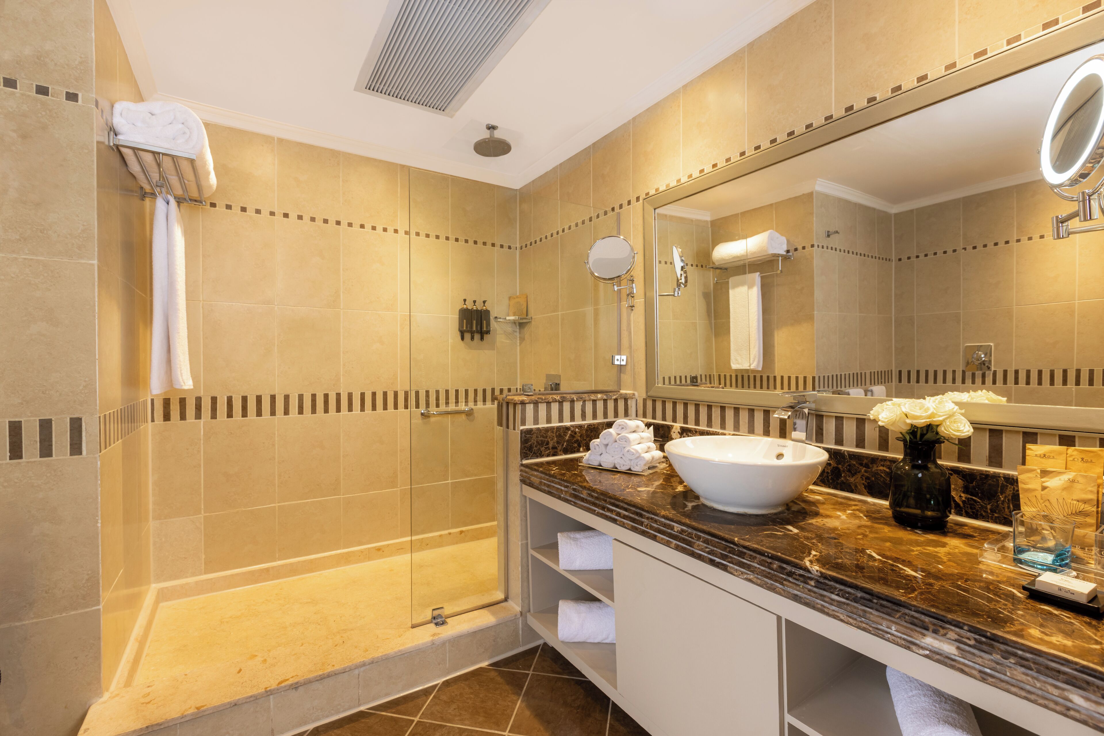 Un baño con ducha a ras de suelo, lavabo, espejo y toallas.