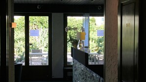 A corridor with a tiled floor, a reception desk with a plant, and a door with a number plate. - Hotel Eremitage (Arlesheim)