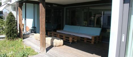 A covered outdoor seating area with wooden benches and a cushioned sofa.