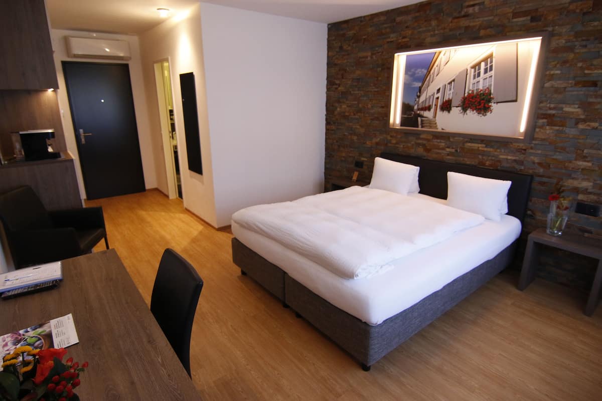 Moderni hotellihuone, jossa on suuri sänky, puinen ruokapöytä ja pieni keittiöalue.