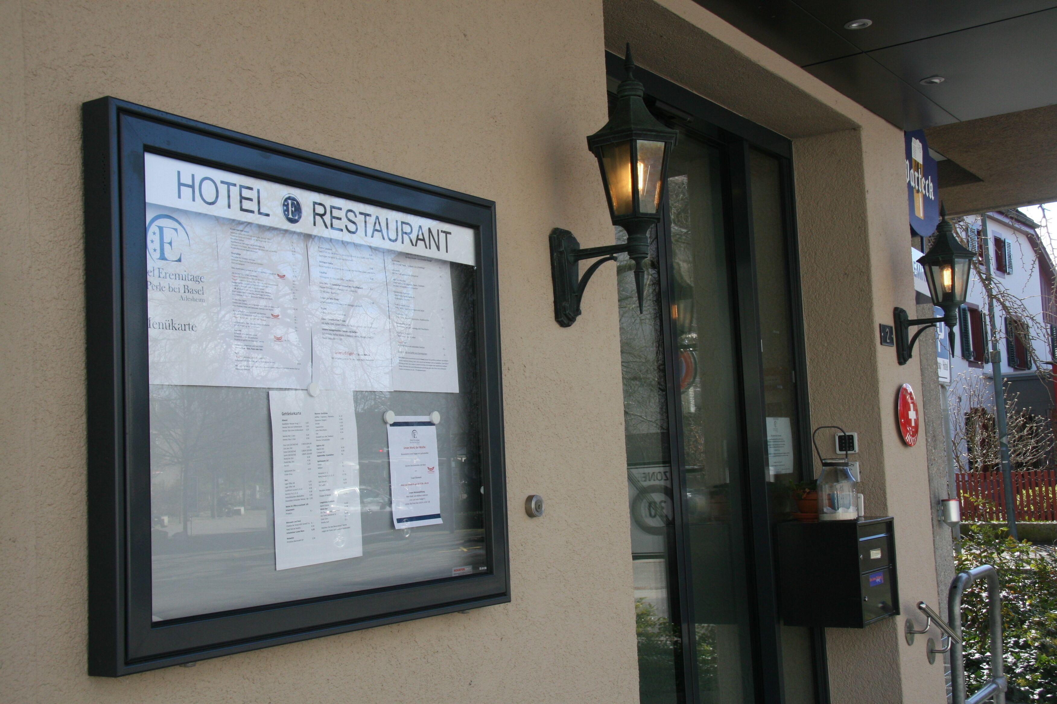 A framed signboard with hotel and restaurant information, a glass door entrance, and a wall-mounted light fixture.