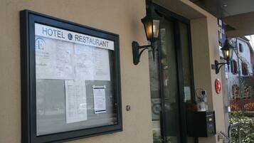 A framed signboard with hotel and restaurant information, a glass door entrance, and a wall-mounted light fixture.