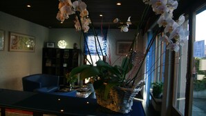 A reception area with a reception desk, a blue sofa, and a potted plant with orchids. - Hotel Eremitage (Arlesheim)