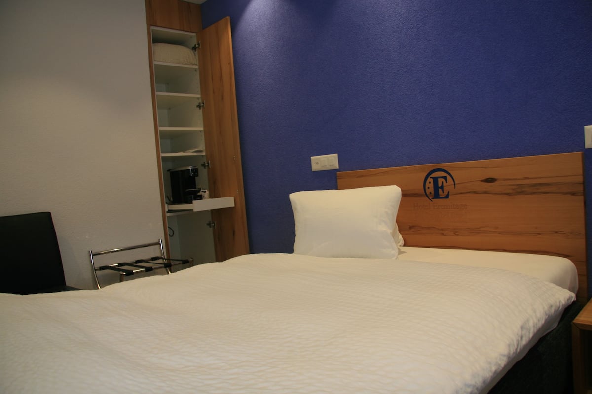 Hotellihuone, jossa on sänky, puinen pääty, hyllykkö ja seinään asennettu valokytkin.
