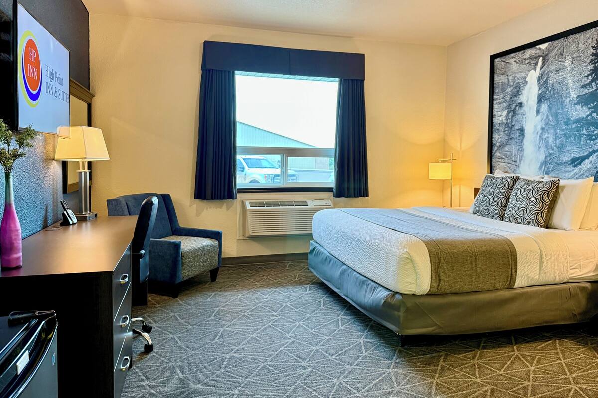 A hotel room with a bed, desk, chair, and a large window.
