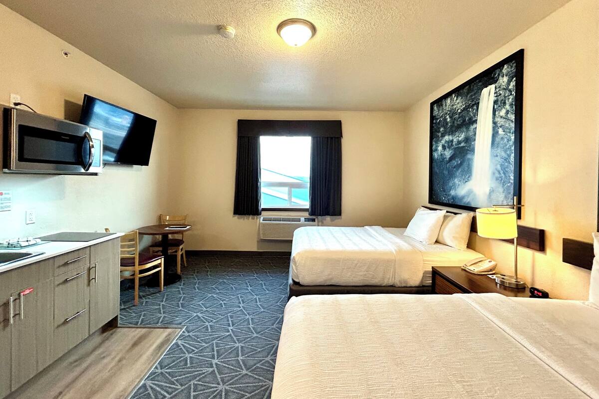 A hotel room with two beds, a desk, a microwave, a television, and a painting on the wall.