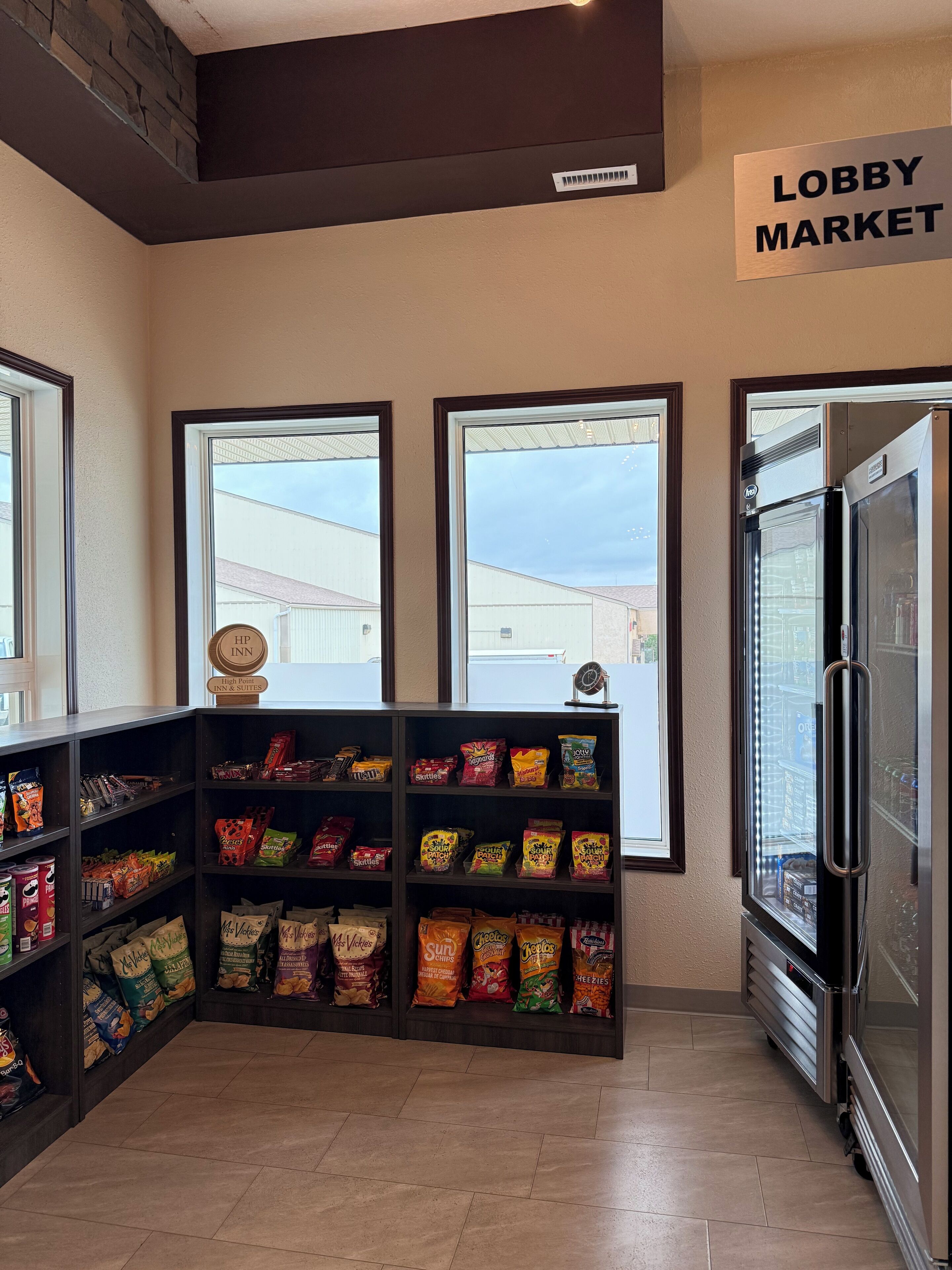 Zona de mercado en el lobby con estantes de snacks y un refrigerador.