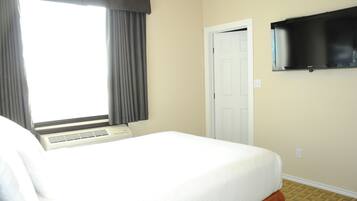 Una habitación de hotel con cama, ventana con cortinas, una puerta y televisor montado.