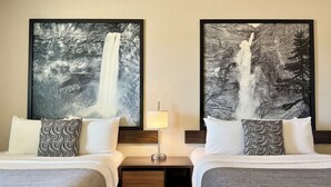 Une chambre d’hôtel avec deux lits, chacun agrémenté d’un oreiller à motifs, une table de chevet avec une lampe, et deux grandes peintures en noir et blanc représentant des cascades, accrochées au mur.