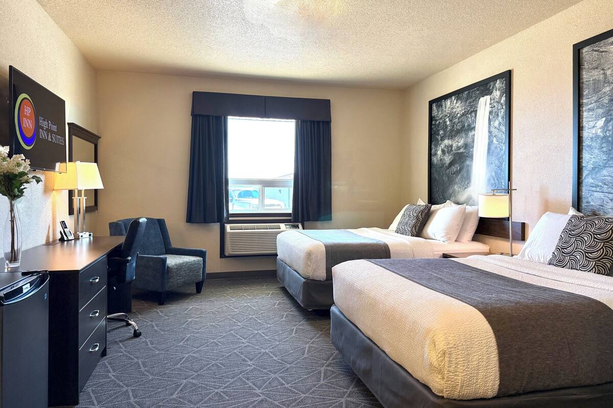 A hotel room with two beds, a desk, a chair, and a large window.