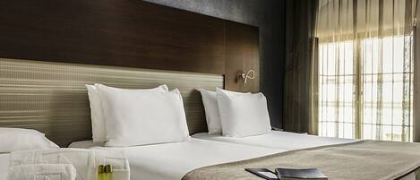 Una habitación de hotel con una cama grande, cabecera y una ventana con cortinas.