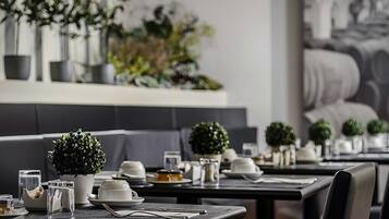 Un ristorante con tavoli apparecchiati per la cena, piante in vaso e un arredamento dal design moderno.