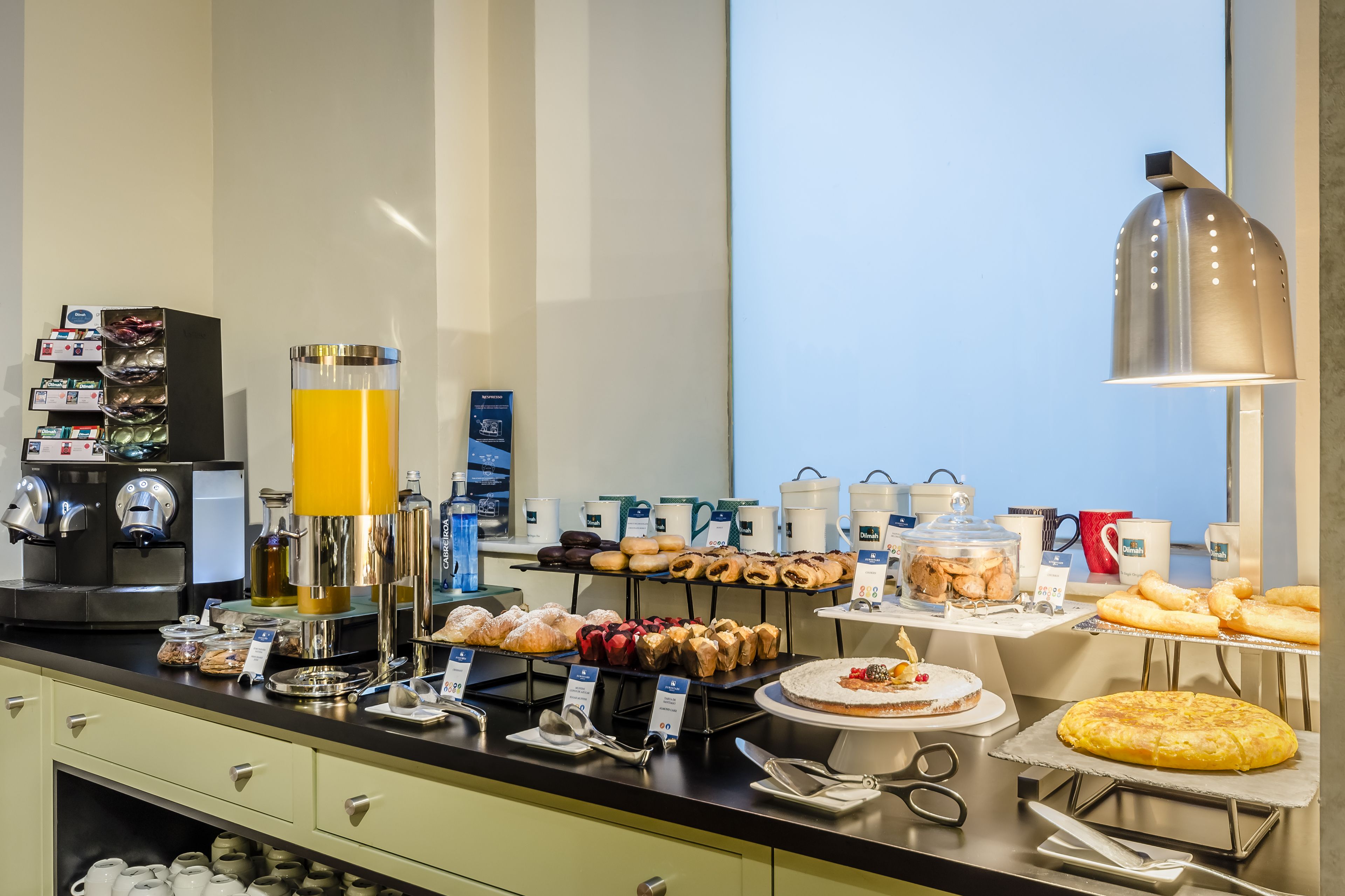 A breakfast buffet with various pastries, a coffee machine, and a juice dispenser.
