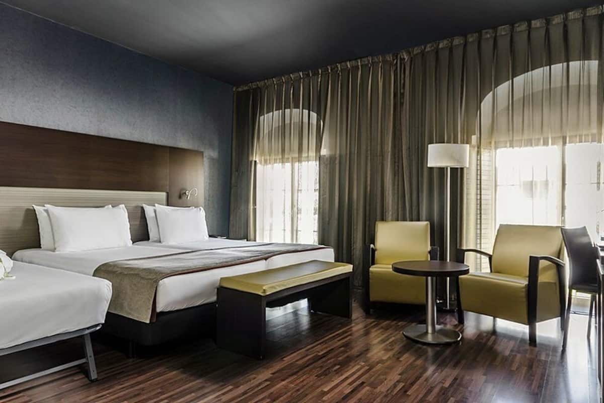 Ein Hotelzimmer mit einem großen Bett, zwei Einzelbetten, einem Schreibtisch, einem Stuhl und einer Lampe.