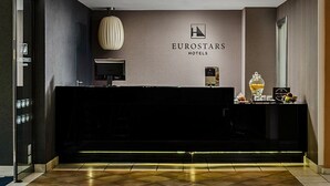 Een modern hotel ontvangstgedeelte met een donker receptiebalie, een groot logo erboven en een wandklok.
