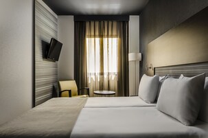 A hotel room with a bed, a TV mounted on the wall, a round table, and a chair.