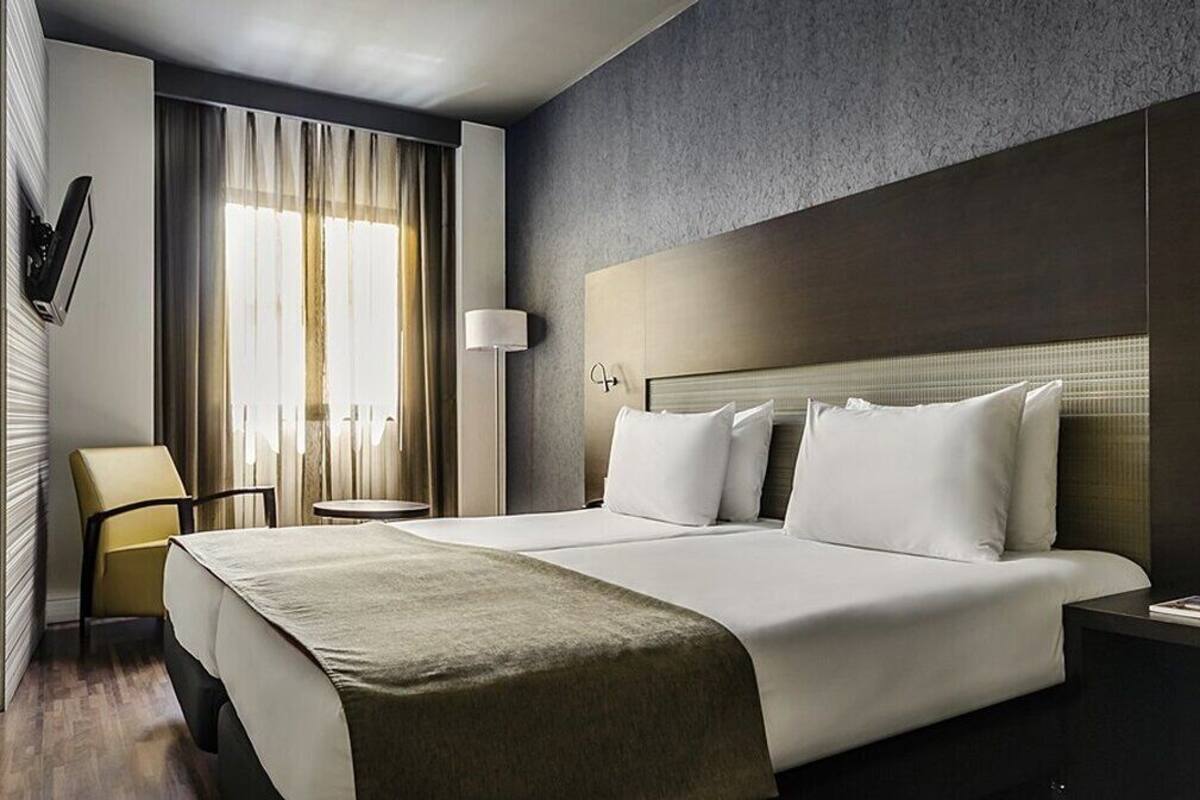Ein modernes Hotelzimmer mit einem großen Bett, einem Nachttisch, einem Sessel und einem Fenster mit Vorhängen.