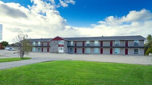 A two-story motel with a red and grey facade, multiple rooms with red doors, and a parking lot in front.